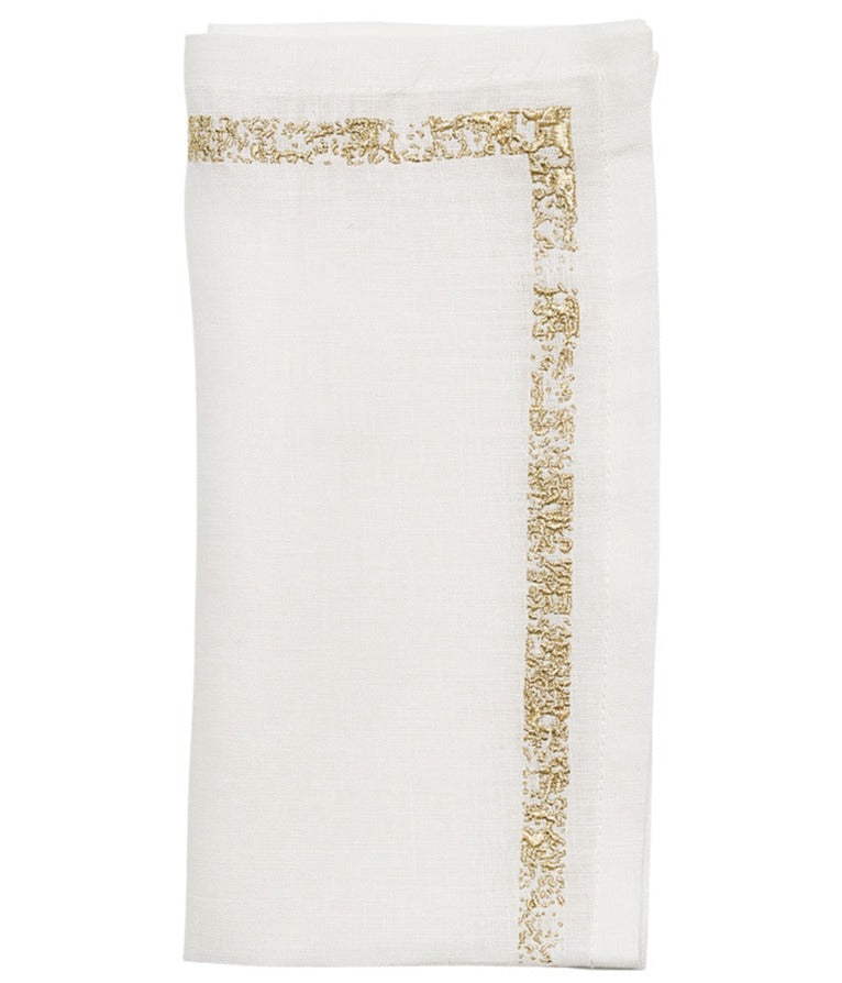 The Kim Seybert Impression Napkin Set features white linen napkins with a decorative gold embroidered border, folded neatly.