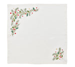 The Christmas Carol Table Linen Collection by Kim Seybert features a white cloth napkin embroidered with green pine branches and red-gold berries in two corners, ideal for festive holiday table settings.