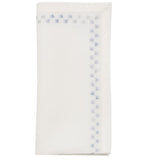 The Starry Night Napkin Set by Kim Seybert features folded white linen napkins with shimmering metallic blue floral embroidery along the border, adding a delicate, elegant touch to any table setting.