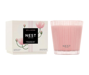A pink Nest Himalayan Salt & Rosewater Candle from the Candle Collection sits by its matching floral box, infusing the air with soothing rosewater and a hint of amber.