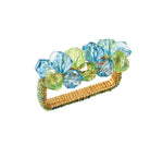 The Pop Rocks Napkin Ring by Kim Seybert features a gold rectangular design with large faceted blue and green beads, adding playful sparkle reminiscent of a bold statement bracelet.
