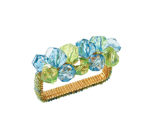 The Pop Rocks Napkin Ring by Kim Seybert features a gold rectangular design with large faceted blue and green beads, adding playful sparkle reminiscent of a bold statement bracelet.
