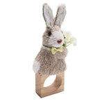 Brighten your table with the Kim Seybert Easter Bunny Napkin Ring, featuring a sisal hemp bunny with yellow bow tie, blue collar, and white flowers on a wooden base—perfect for spring decor.
