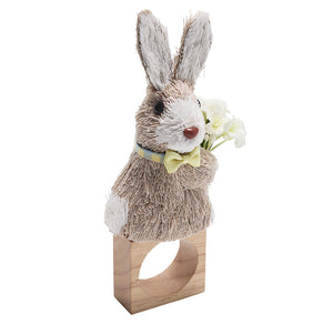 Brighten your table with the Kim Seybert Easter Bunny Napkin Ring, featuring a sisal hemp bunny with yellow bow tie, blue collar, and white flowers on a wooden base—perfect for spring decor.