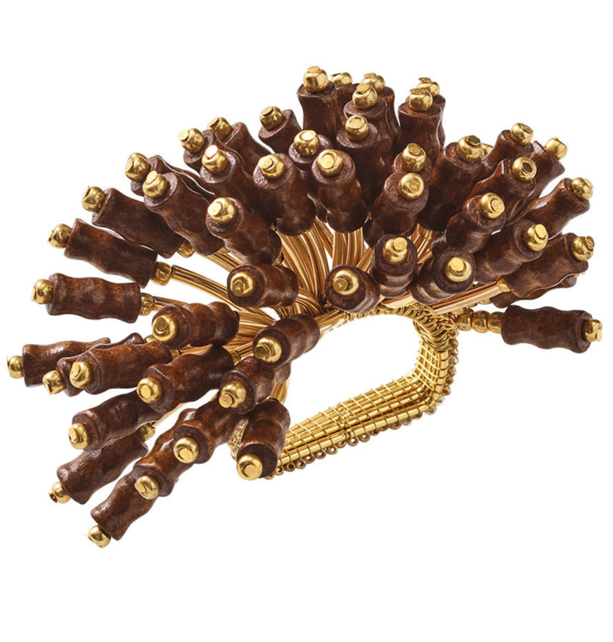 The Kim Seybert Royal Palm Napkin Ring features multiple wooden handles with gold tips, arranged in a circle and connected to a beaded base, evoking tropical elegance.