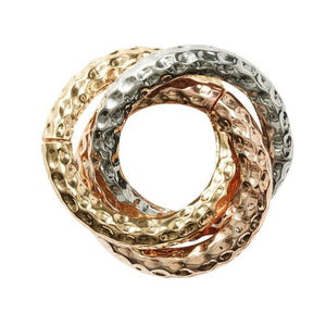 The Kim Seybert Trinity Napkin Ring Set features three interlocking hand-hammered metal rings in gold, rose gold, and silver tones, creating an elegant and modern accent for any table setting.