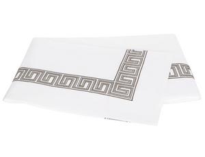 Two folded white sheets from Matouk’s Ophelia Bedding Collection, Mocha, featuring an elegant black and gray Greek key border and crafted from luxurious 520 thread count fabric.