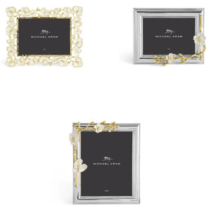 Three rectangular photo frames from the Michael Aram Orchid Frame Collection feature elegant floral designs in golden brass and silver finishes, displayed on a white background.