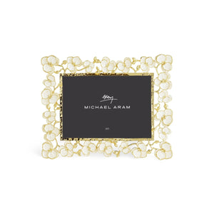 The Orchid Frame Collection by Michael Aram is a rectangular photo frame with gold brass and white enamel floral details, featuring a black placeholder card labeled "Michael Aram.