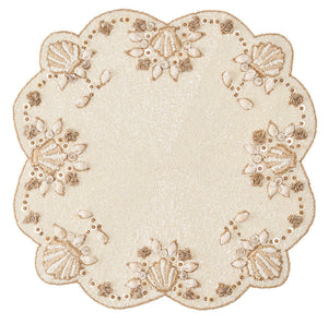 The Kim Seybert Beachcomber Placemat features a round cream and beige design with beaded floral and leaf patterns, scalloped edges, and raffia accents—ideal for a coastal-inspired home.