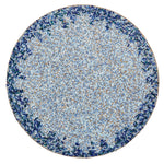 The Kim Seybert Lagoon Placemat showcases a circular mosaic design with a densely patterned blue and brown center accented by cobalt blue beads, bordered by deep ocean-inspired blue and green tones.