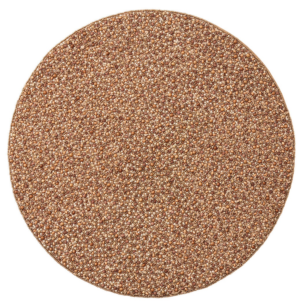 A round pile of small, tan to light brown grains rests on the Kim Seybert Emberfall Placemat, viewed from above against a white background.