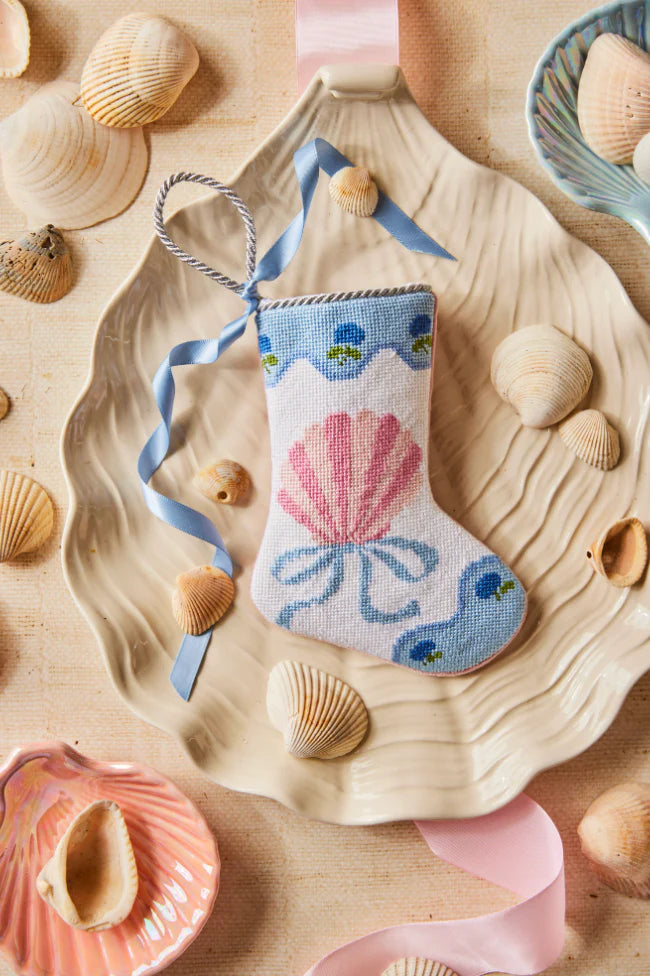 The Let's Shellebrate Needle Point Stocking by Bauble Stockings features a seashell and ribbon design—displayed with shells and ribbons, it adds a Palm Beach Lately touch to your coastal holiday decor.