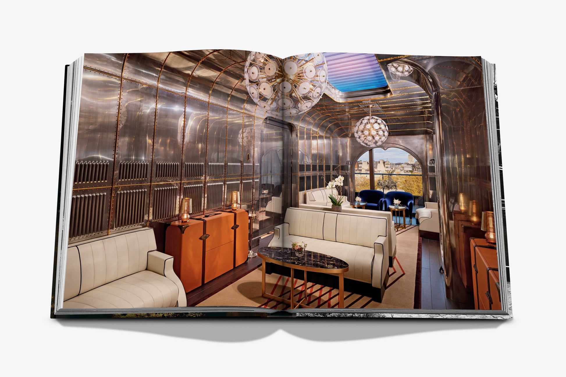 An open photo book by Assouline showcases The Peninsula London, featuring metallic walls, white seating, chandeliers, and city views—capturing the essence of this iconic luxury hotel.