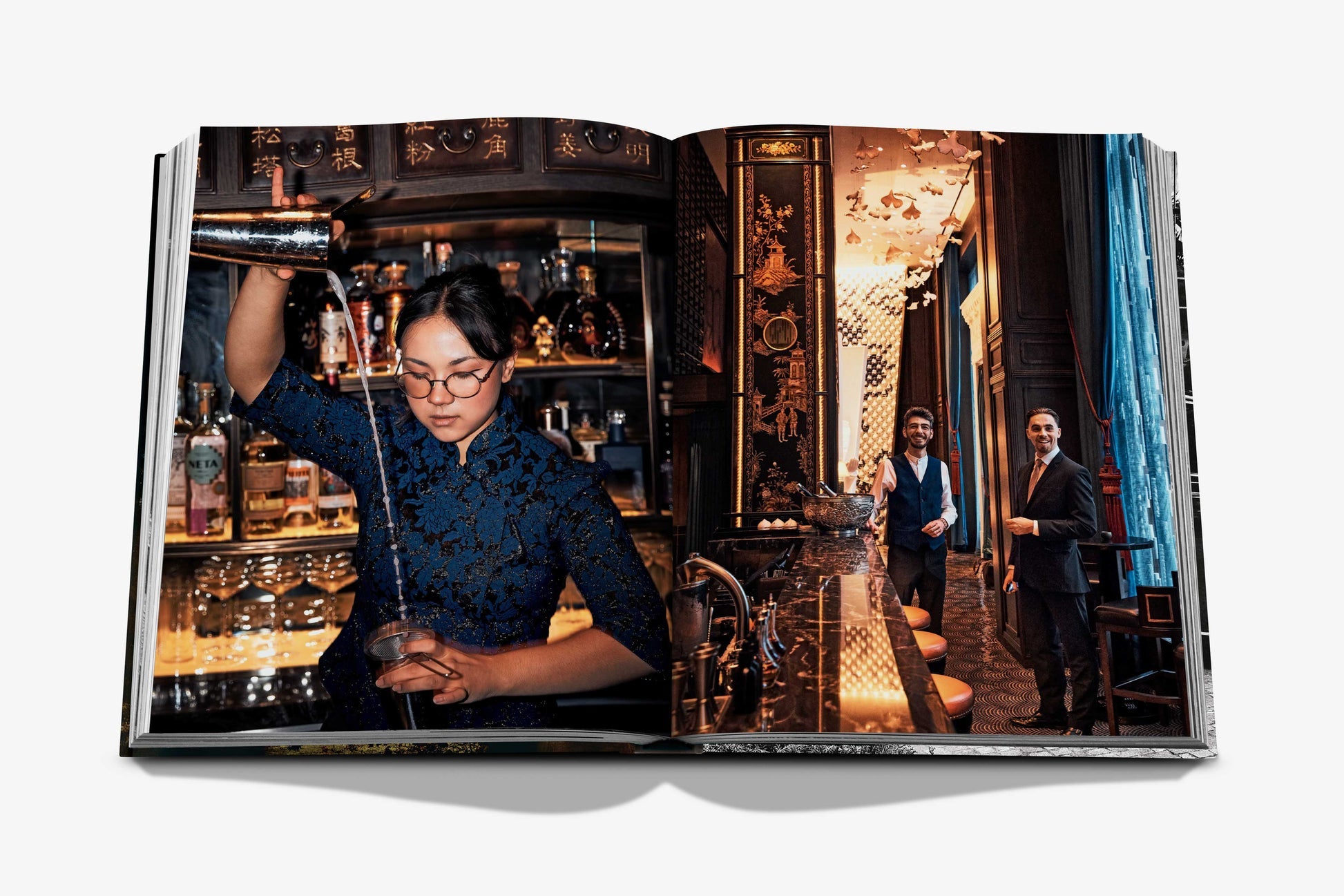 An Assouline book opens to show a bartender pouring a drink and two men at a bar, all set in the elegant, dimly lit ambiance of The Peninsula London, the luxury hotel near Hyde Park.
