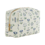 The Luxe Everyday Cosmetic Bag by TRVL Design is a rectangular cream-colored bag featuring a gold zipper and a pattern of small blue and green flowers.
