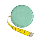 The Graphic Image Leather Tape Measure features a round, mint green case with a yellow tape partially extended, showing measurements in inches—ideal for sewing or crafting projects.