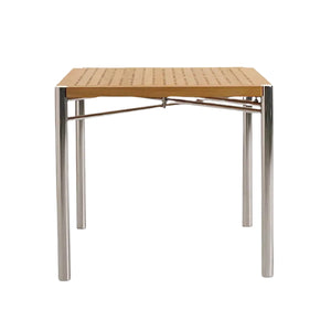 The Sundeck Folding Table by Summit Furniture features a square perforated teak top and four cylindrical marine-grade stainless steel legs, inspired by classic campaign furniture, shown front view against a white background.