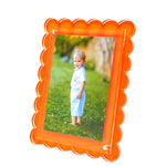 A framed photo of a child on green grass, showcased in Tara Wilson Designs’ best-selling Scallop Frame Collection—an orange, scalloped-edge lucite frame that adds brightness to any space.