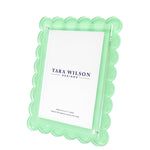 The Scallop Frame Collection by Tara Wilson Designs features a mint green lucite photo frame with scalloped edges, blending elegance and modern style. This upright best-seller displays a "Tara Wilson Designs" placeholder card.