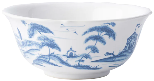 From Juliska’s Country Estate Delft Blue Dinnerware Collection: a white porcelain bowl adorned with a blue pastoral scene of trees, birds, buildings, tents, and countryside charm near a horse stable.
