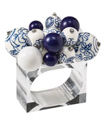 The Kim Seybert Cloud Napkin Ring, featuring a clear Lucite band adorned with blue, white, and patterned ceramic and acrylic baubles, brings an artful accent to your table setting.