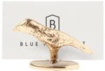 The Hailey Gold Place Card Holder Set by Blue Pheasant features a small, gold-colored bird sculpture with a lustrous finish standing on an oval base, displayed in front of a card with “BLUE B” partially visible.