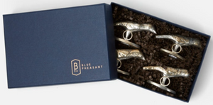 A blue-lidded box with "Blue Pheasant" text and logo contains four Zachary tarnished silver bird-shaped place card holders, nestled in brown shredded paper.