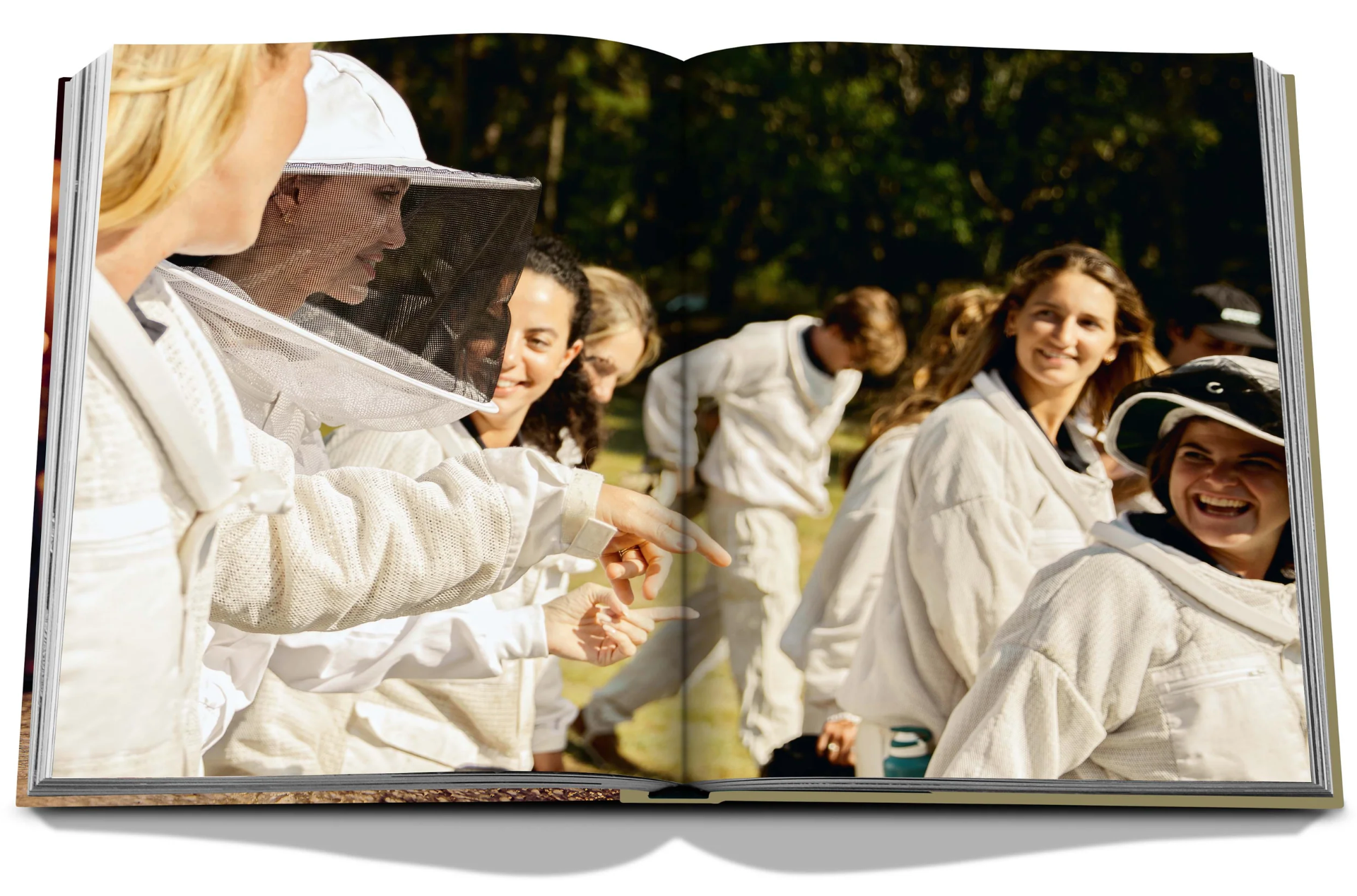 A group of people dressed in white beekeeping suits, some with veiled hats, are gathered together outdoors, engaging in conversation and smiling, reminiscent of Assouline's celebrated Bee Bottle collection featuring Guerlain An Imperial Icon.