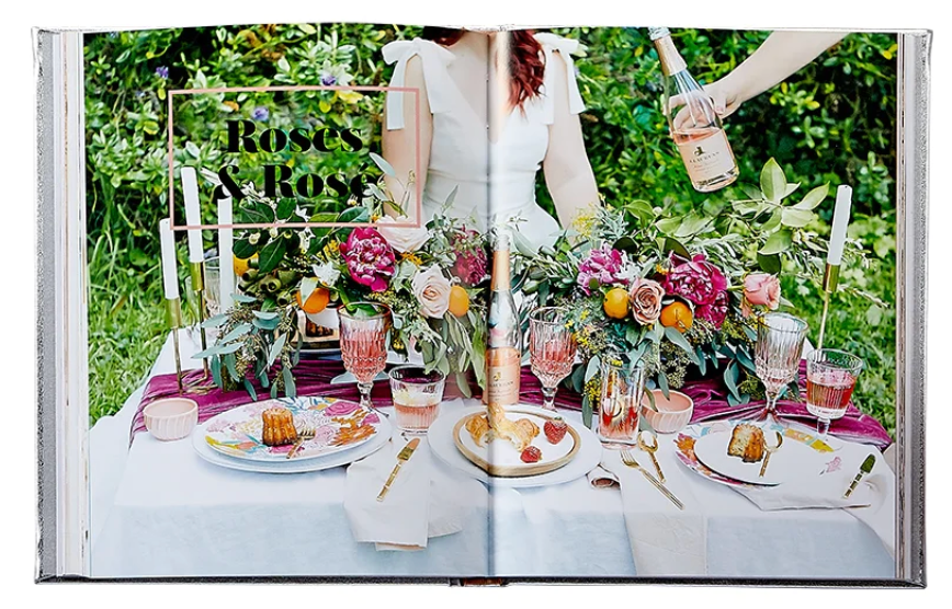 A table set for a meal showcases flowers, dishes, and glasses next to a served bottle with the text "Roses & Rosé." Get perfect party inspiration from Graphic Image's Celebrate Rose, featuring delightful pink wine rosé cocktails.