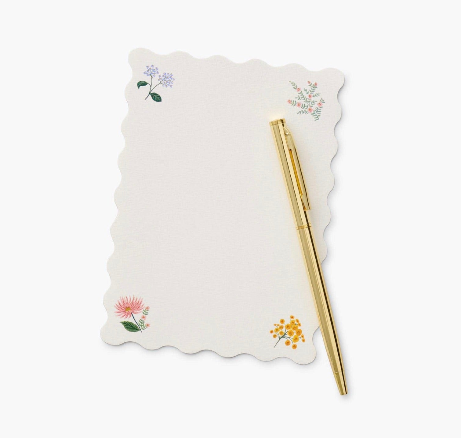 A gold pen rests on a Riffle Paper Co. Dahlia Collection notepad with scalloped edges and small corner floral designs, set against a light background.