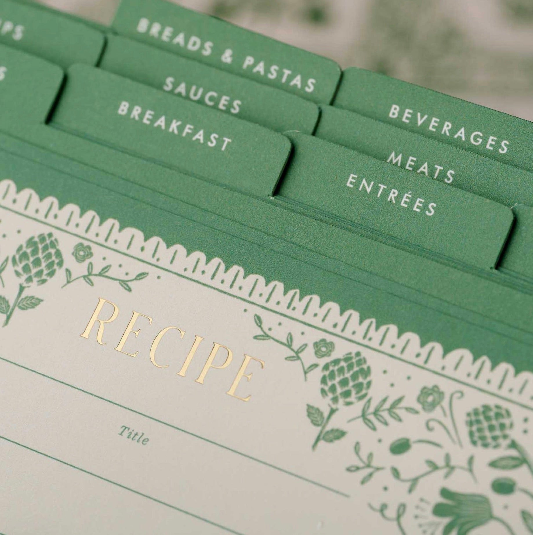 The Artichoke Recipe Tin by Rifle Paper Co. features dividers for breads & pastas, sauces, breakfast, beverages, meats, and entrees—all stylishly organized in a floral box for charming kitchen organization.