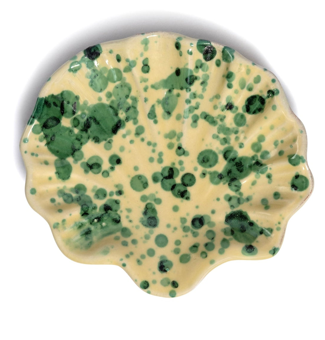 A stylish gift, the Splatter Coquillage Dish Collection by Sharland England is handmade in Italy—a ceramic plate with a wavy edge, yellow base, and irregular green splatter pattern.