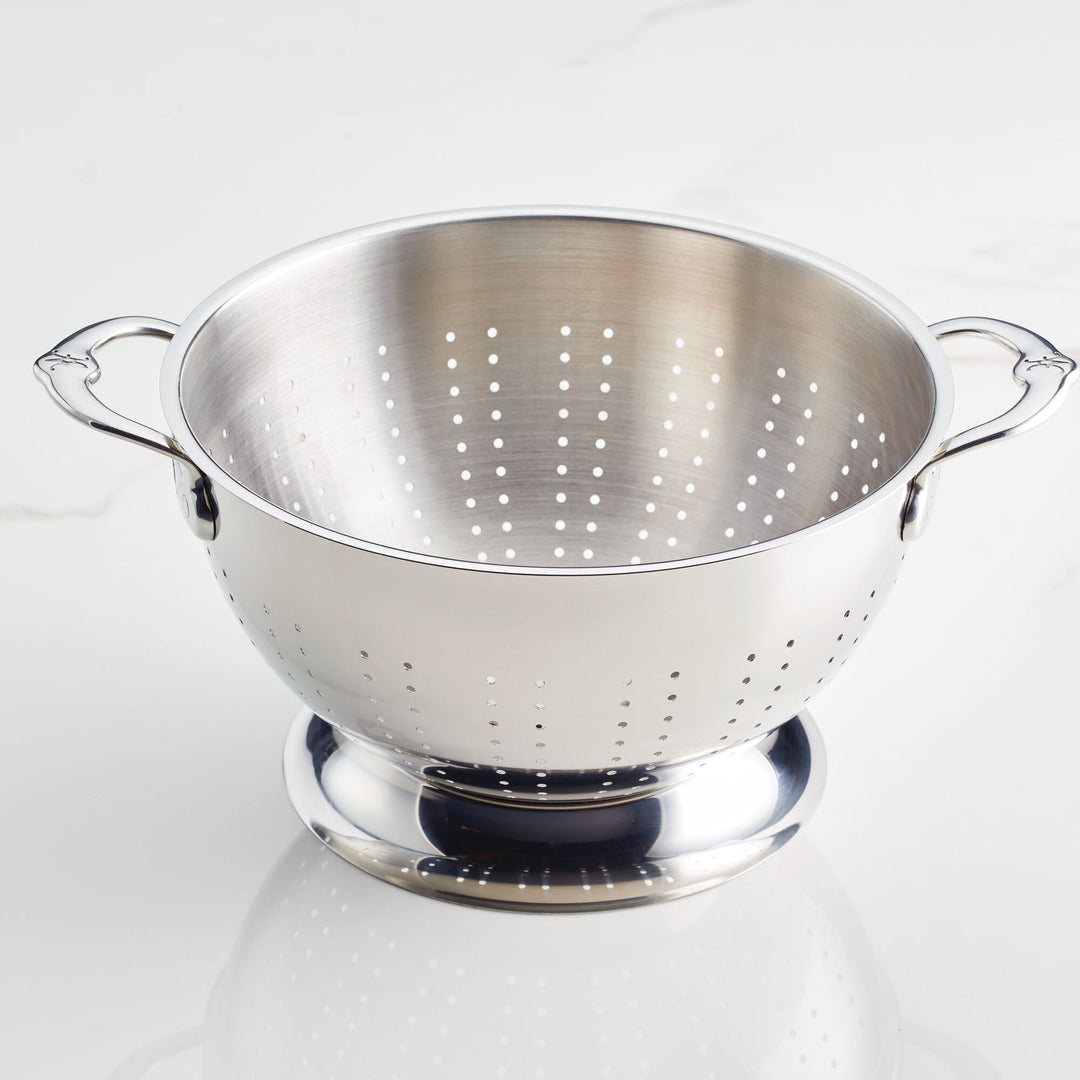 The Hestan Provisions Stainless Steel Colander 2-Piece Set, featuring ergonomic handles for comfort and superior drainage, rests on a white surface.