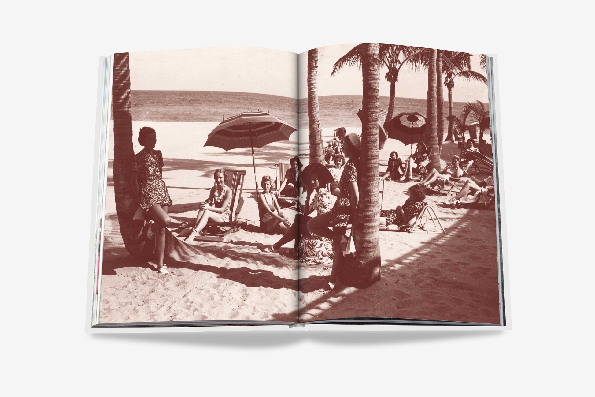 An open book from Assouline, entitled The Surf Club, showcases a sepia-toned image of people unwinding on a beach beneath umbrellas and palm trees, evoking the luxurious atmosphere of Miami's renowned Surf Club. The sea can be seen in the distance.