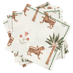 The Matouk Tiger Palm Tabletop Collection features white napkins with Schumacher-inspired borders, decorated with tigers, palm trees, and jungle motifs.