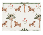 The Matouk Tiger Palm Tabletop Collection features a rectangular placemat adorned with Schumacher's jungle motif—tigers, palm trees, and red flowers—set on a white background with a green border.