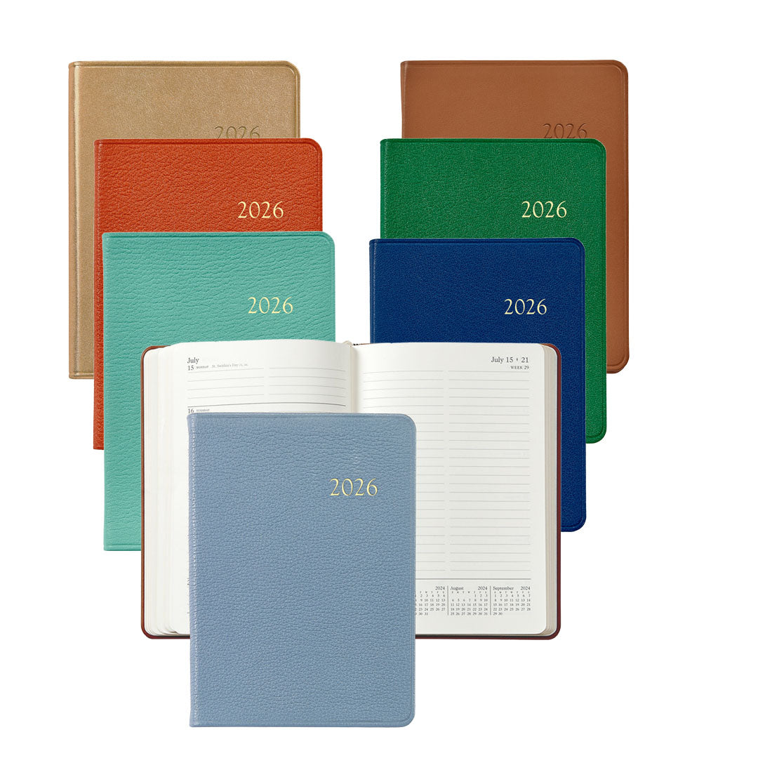 Seven Graphic Image 2026 Weekly Journal Planner Collection notebooks in assorted colors are shown, with one open to reveal lined appointment pages and a convenient calendar.