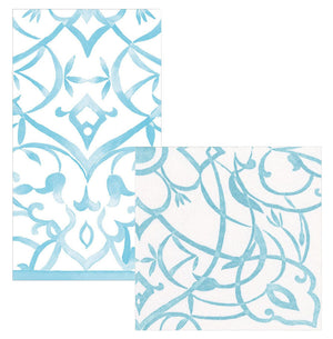 Two white paper linen napkins from Caspari's Algarve Aqua Collection, featuring light blue ornate, symmetrical patterns and flourishes, are displayed side by side.