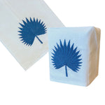 Haute Home’s Palm Leaf Bath Collection, Blue, includes a white Italian linen napkin and hand-embroidered tissue box cover, both adorned with a blue palm leaf motif.