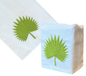 The Haute Home Palm Leaf Bath Collection in green features hand-embroidered Italian linen napkins, a matching napkin holder, and a tissue box cover—all adorned with a white and green palm leaf design.
