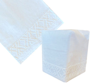 The Lido Bath Collection Tissue Box Cover by Haute Home features white Italian linen with a subtle geometric hand-embroidered pattern along the bottom edge, shown both flat and in use.