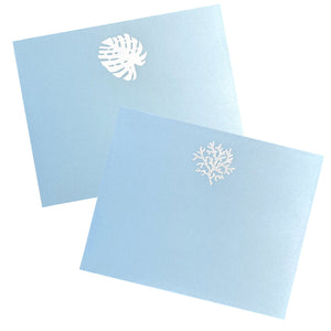 Two Bristol Vellum Blue cards from Black Ink's Large Blue Note Pad Collection, featuring white monstera leaf and coral designs, rest on a white background.