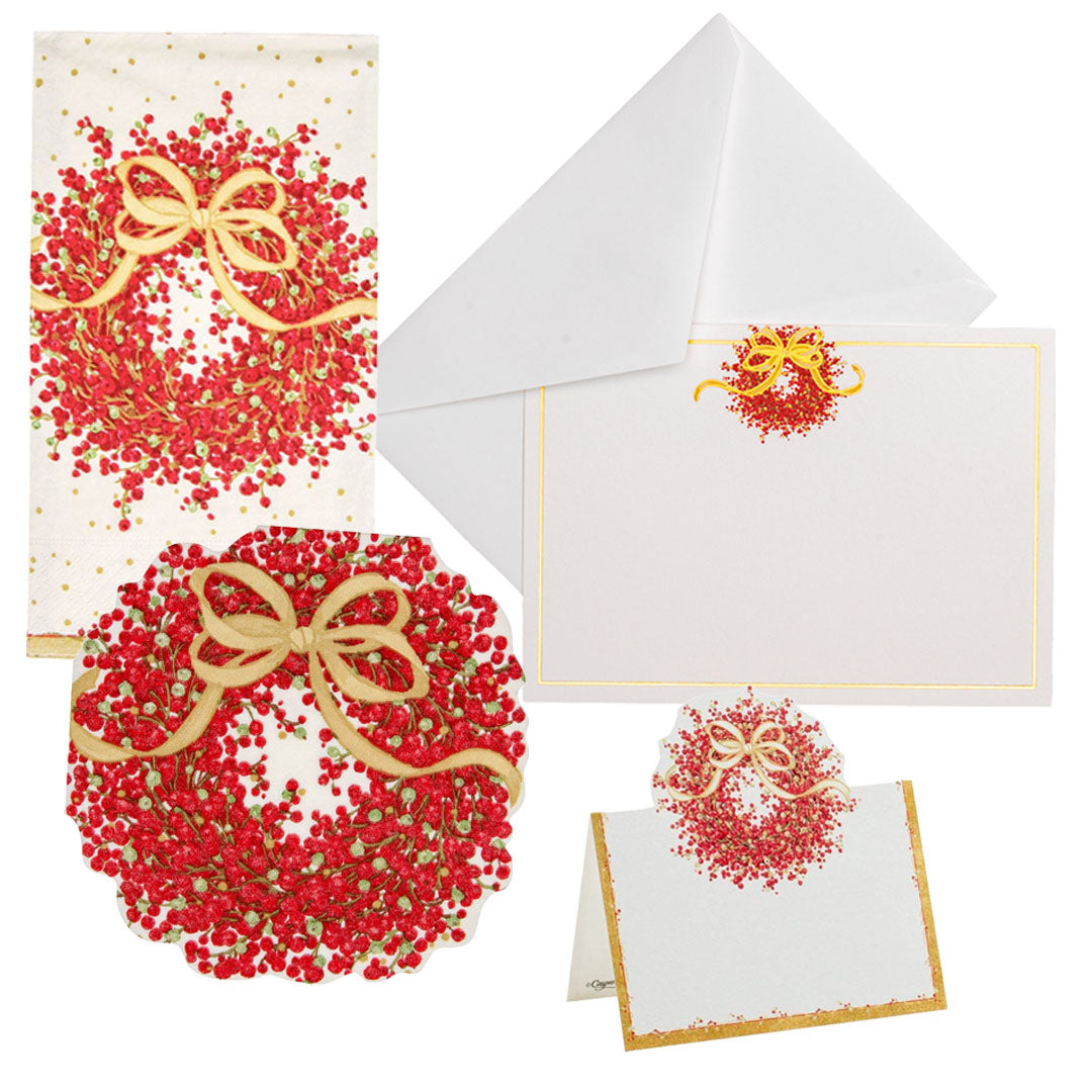 The Caspari Pepperberry Tabletop and Stationery Collection features white envelopes, cards, and cocktail napkins adorned with a festive red and gold wreath design.
