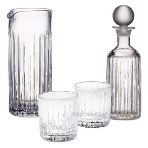 The Montpelier Drinkware Collection by Simon Pearce features a clear glass pitcher, two Double Old-Fashioned glasses, and a decanter with round stopper—all hand-blown with vertical ridges for an elegant, premium touch.