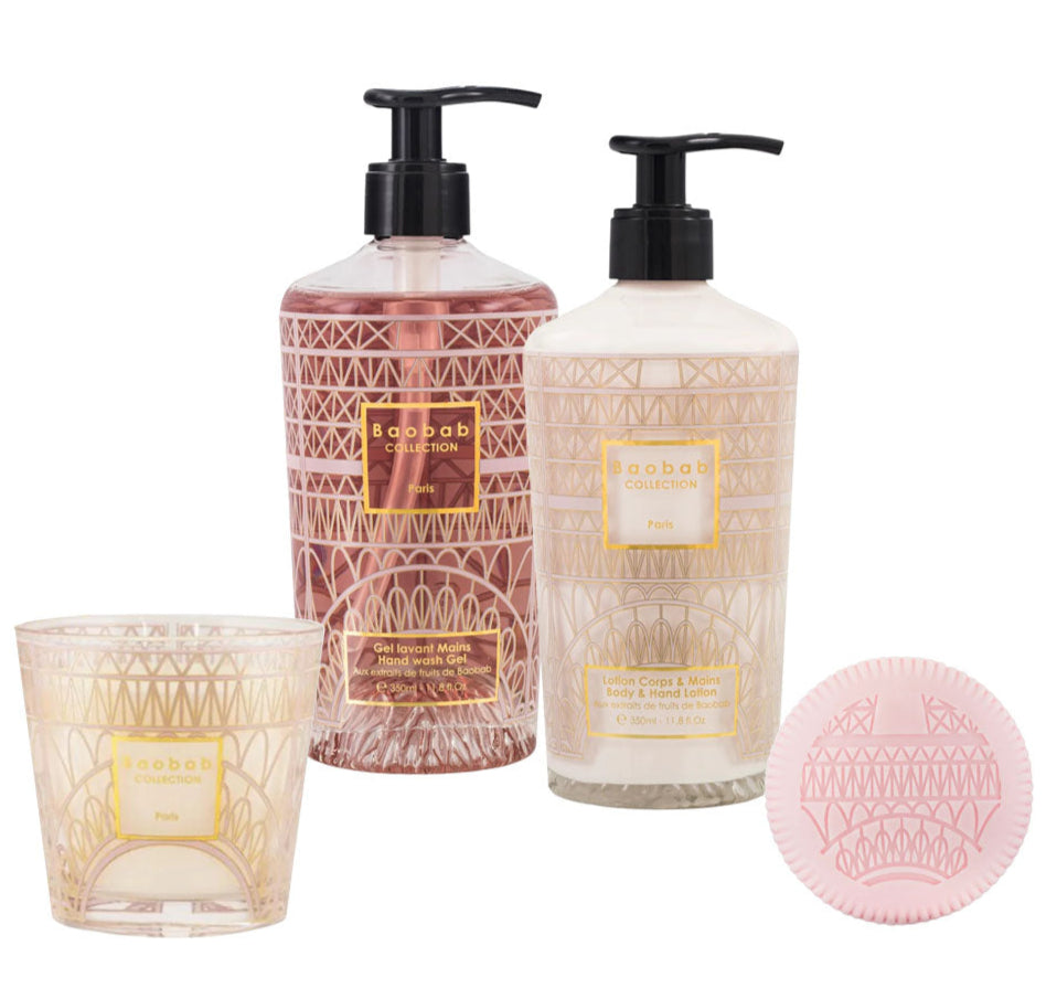 The Baobab Collection Paris Body Wellness Collection features a candle, lotion, liquid hand soap, and round pink soap with gold geometric designs, all infused with a Paris scent of wisteria and chestnut bloom.