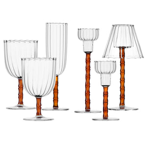 Six clear goblets from the Rivoli Drinkware and Tealight Collection by Ichendorf Milano feature ribbed glass and amber-toned, bamboo-inspired stems—an elegant showcase of hand-crafted design against a white background.