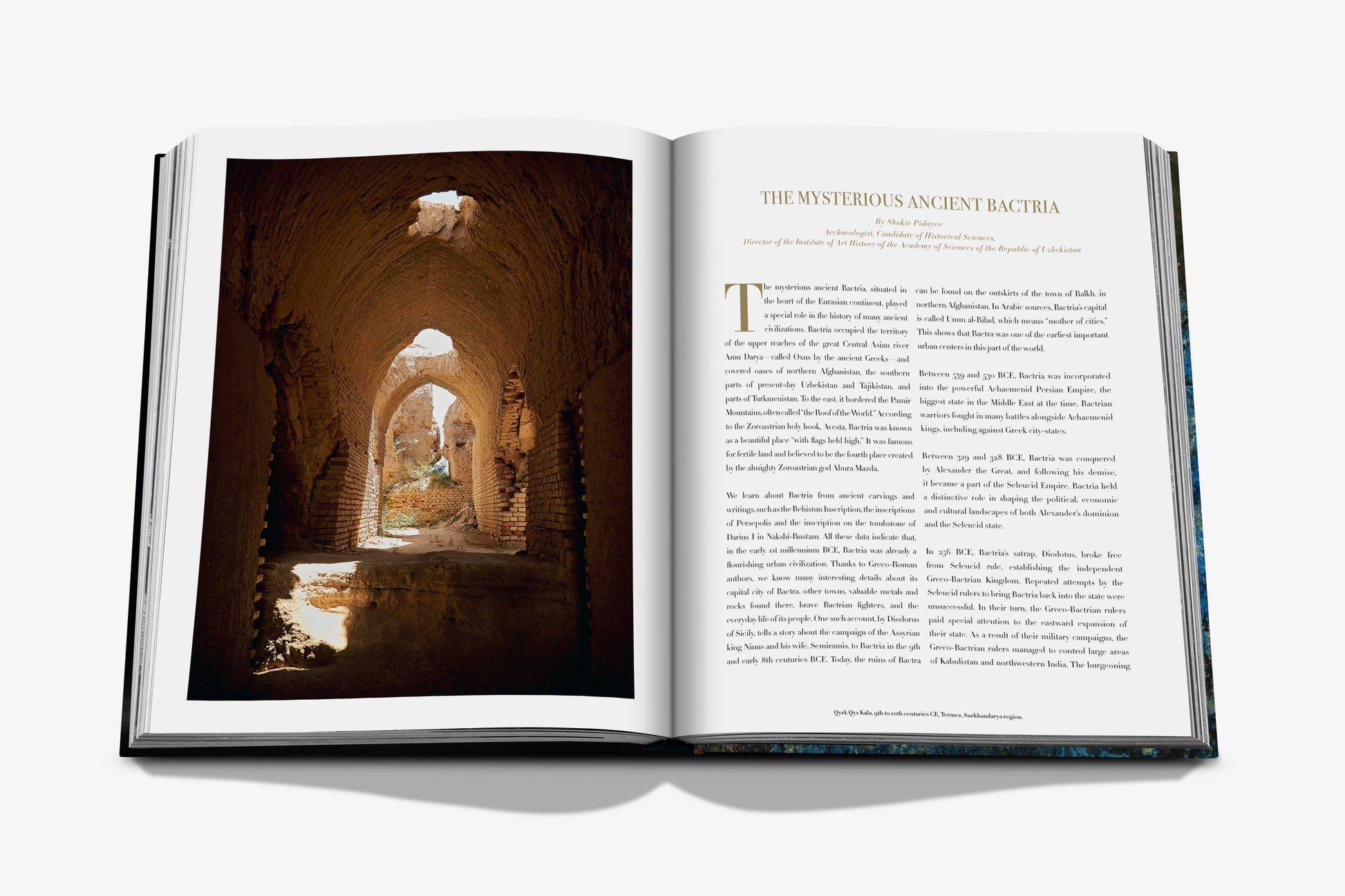 A copy of "Uzbekistan: Masterpieces of the Silk Road" by Assouline displays an article titled "The Mysterious Ancient Bactria" on the right page, accompanied by a photo of a historic, arched hallway on the left. This exploration into Uzbekistan's rich history reveals its significant role in the Silk Road and recent archaeological discoveries that uncover long-lost secrets.