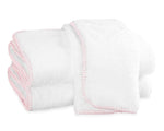 Three white towels with light pink terry whipstitching from the Matouk Whipstitch Bath Collection are neatly folded and stacked on a white background.