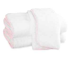 Three white towels with light pink terry whipstitching from the Matouk Whipstitch Bath Collection are neatly folded and stacked on a white background.